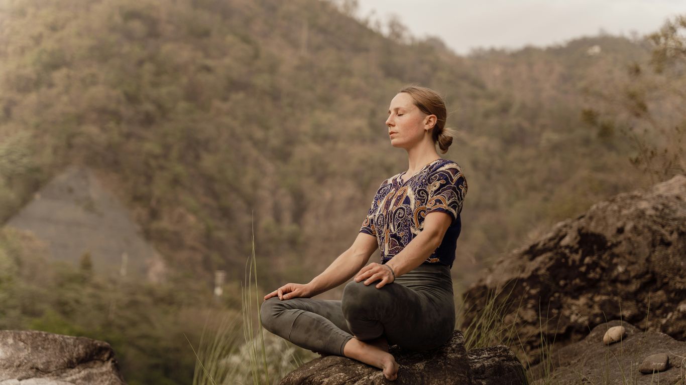a woman sitting on top of a rock in a yoga position