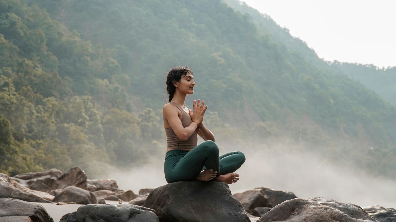 a woman sitting on top of a rock next to a river