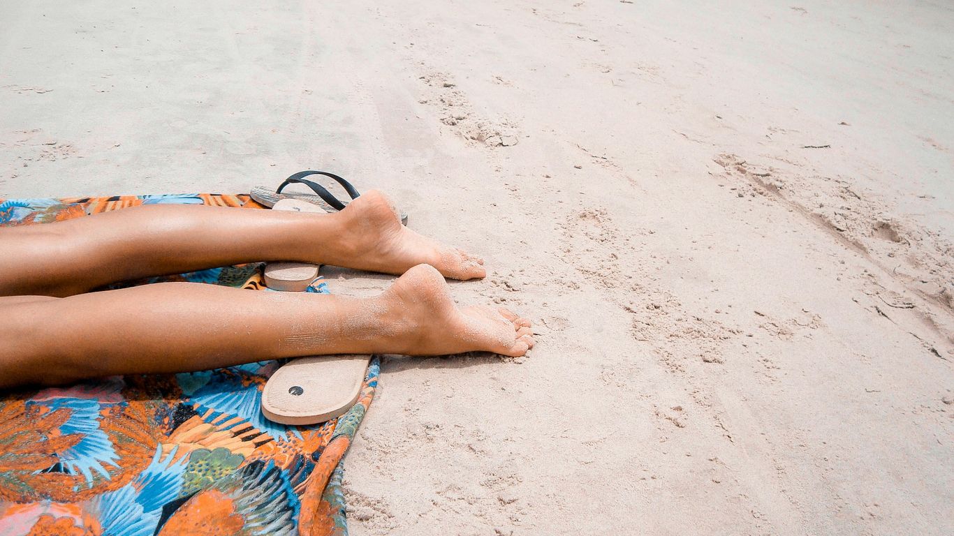 bare foot person lying on orange textile on brown sand during daytime