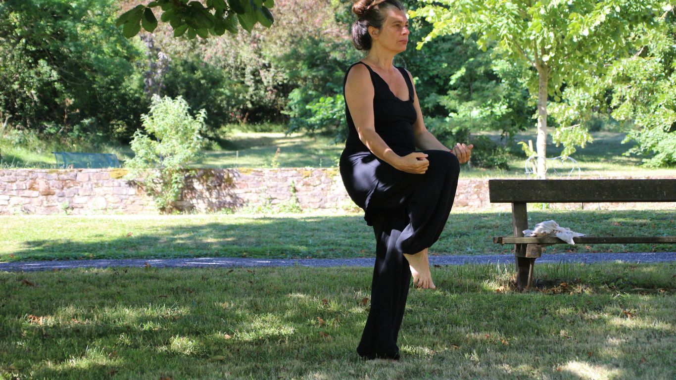 woman in black tank top and black pants sitting on brown wooden bench under green tree