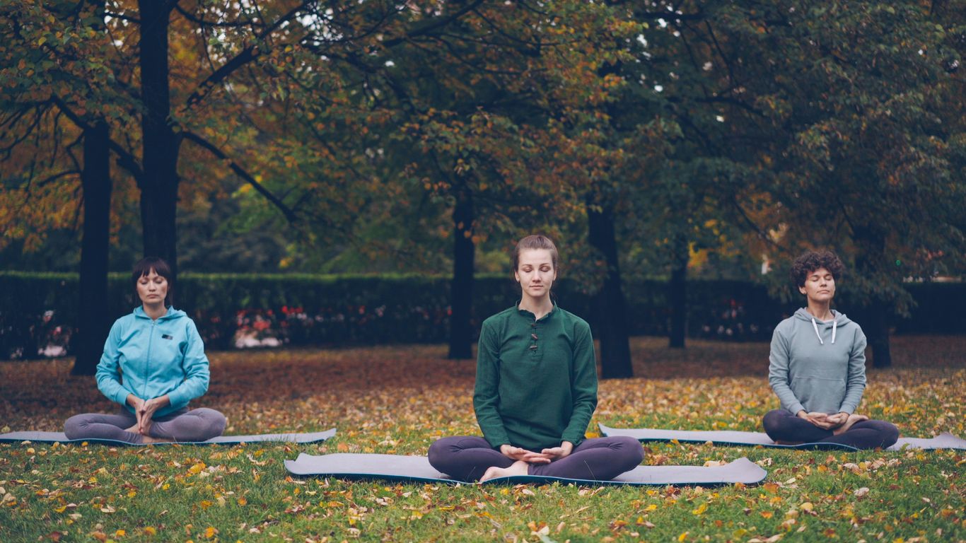 Three people meditating in a park during autumn.