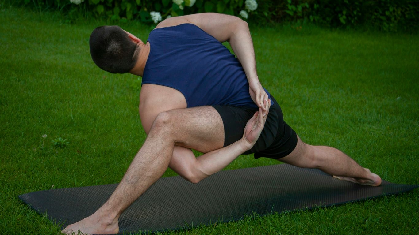 man in blue tank top and black shorts lying on black mat on green grass field