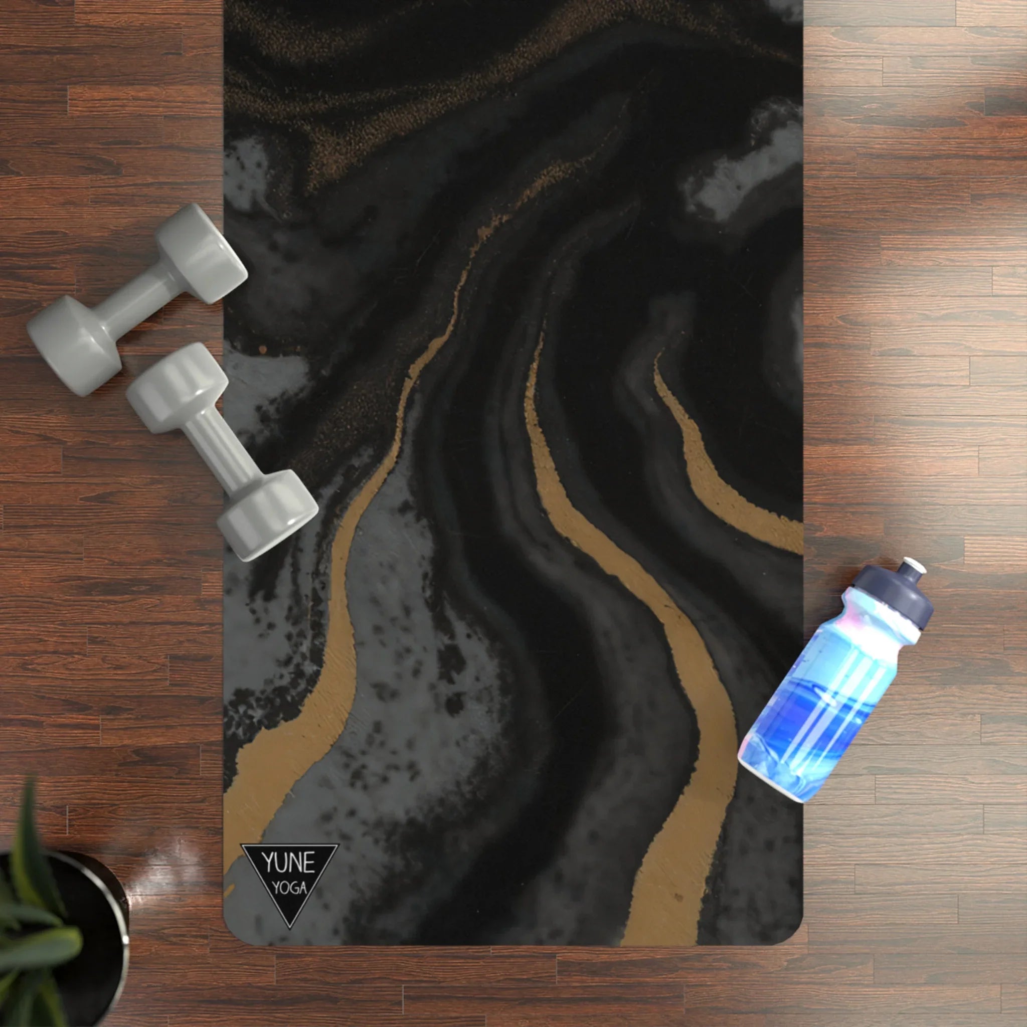 Black and gold marble yoga mat on wooden floor with gray dumbbells and blue water bottle