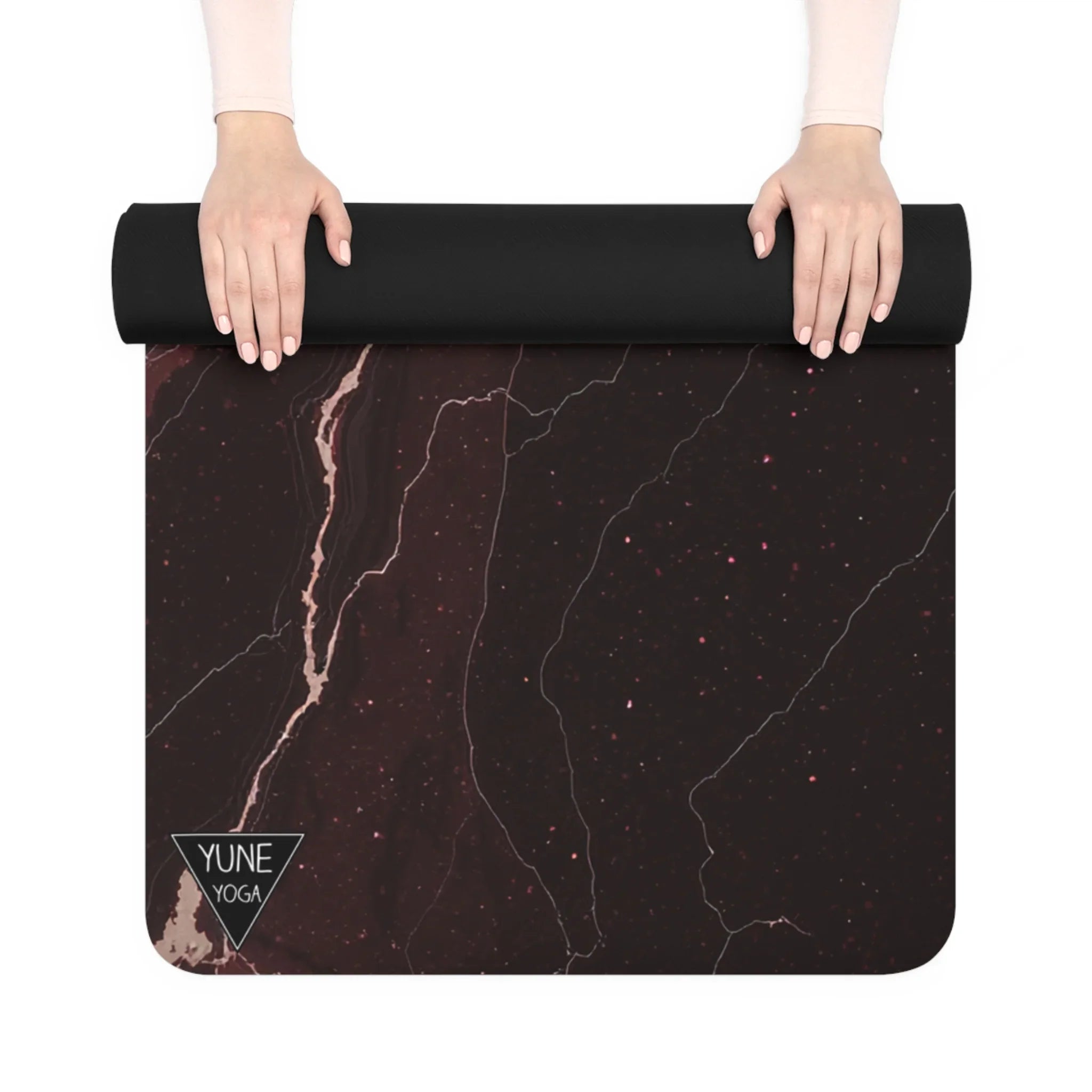 Hands rolling out a black marbled yoga mat with pink accents on a white background