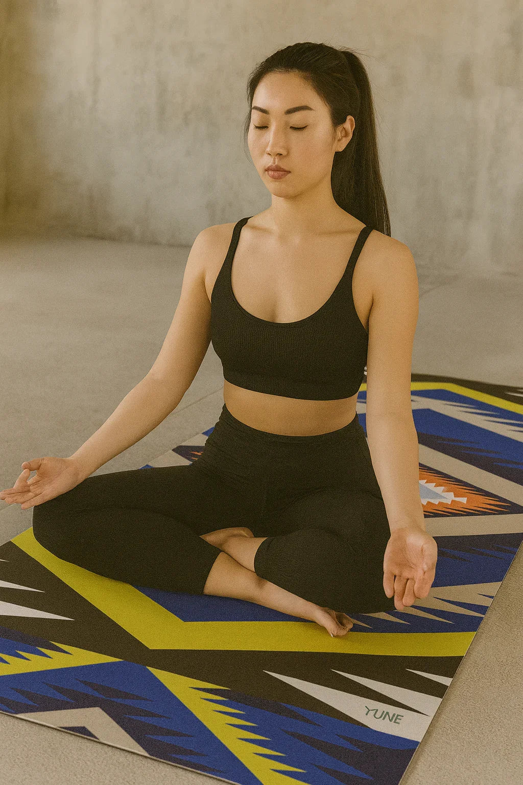 Woman in black athletic wear sitting in a yoga pose on a colorful mat.