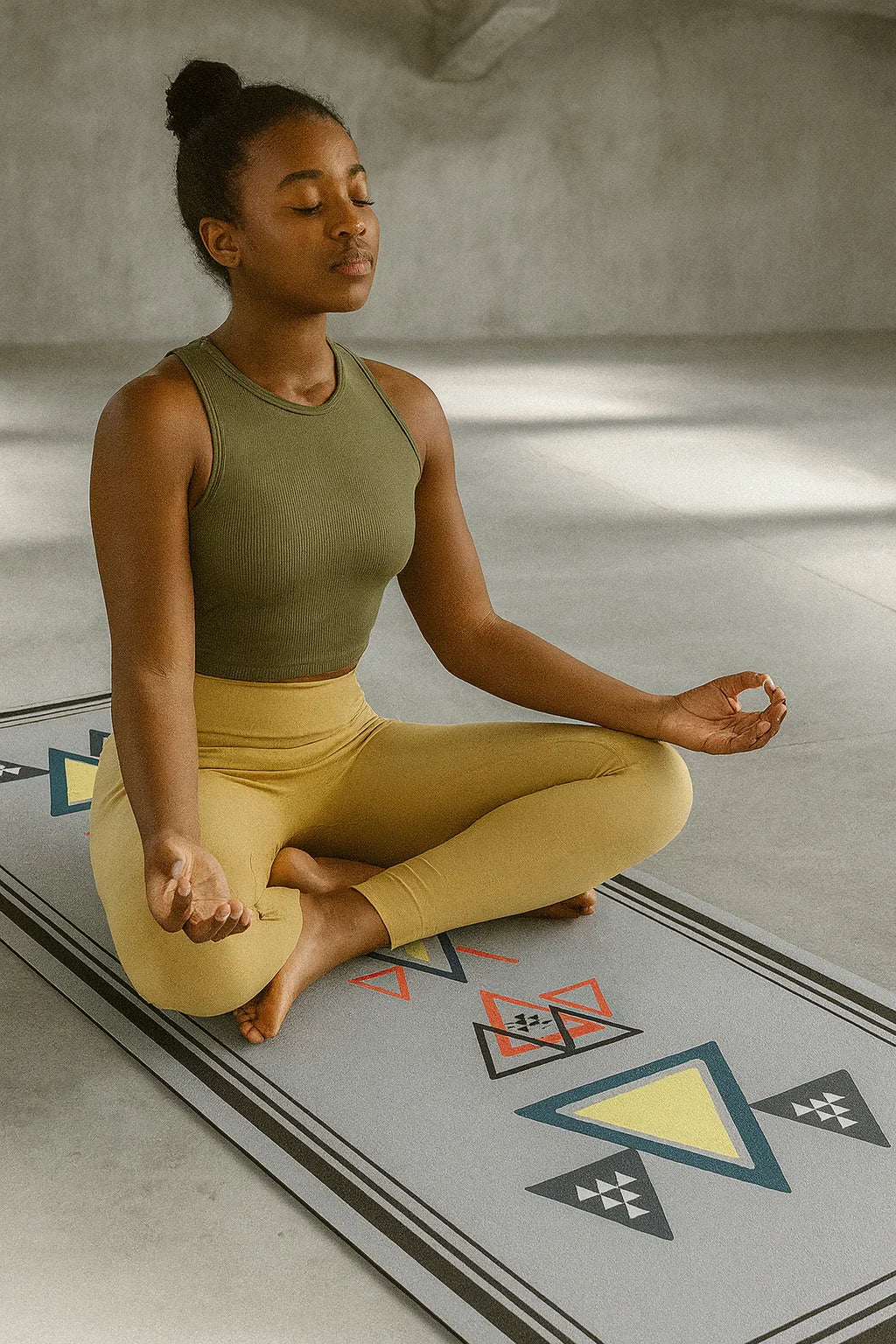 Woman meditating on a yoga mat with geometric patterns in a room with a textured wall.