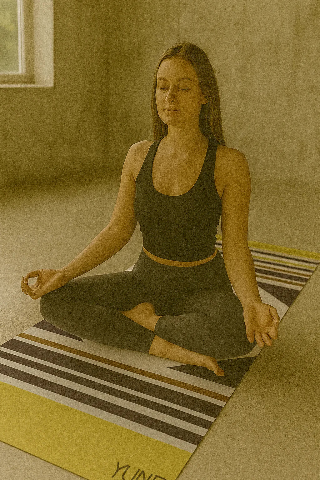 Woman practicing yoga on a striped mat in a room with a window.