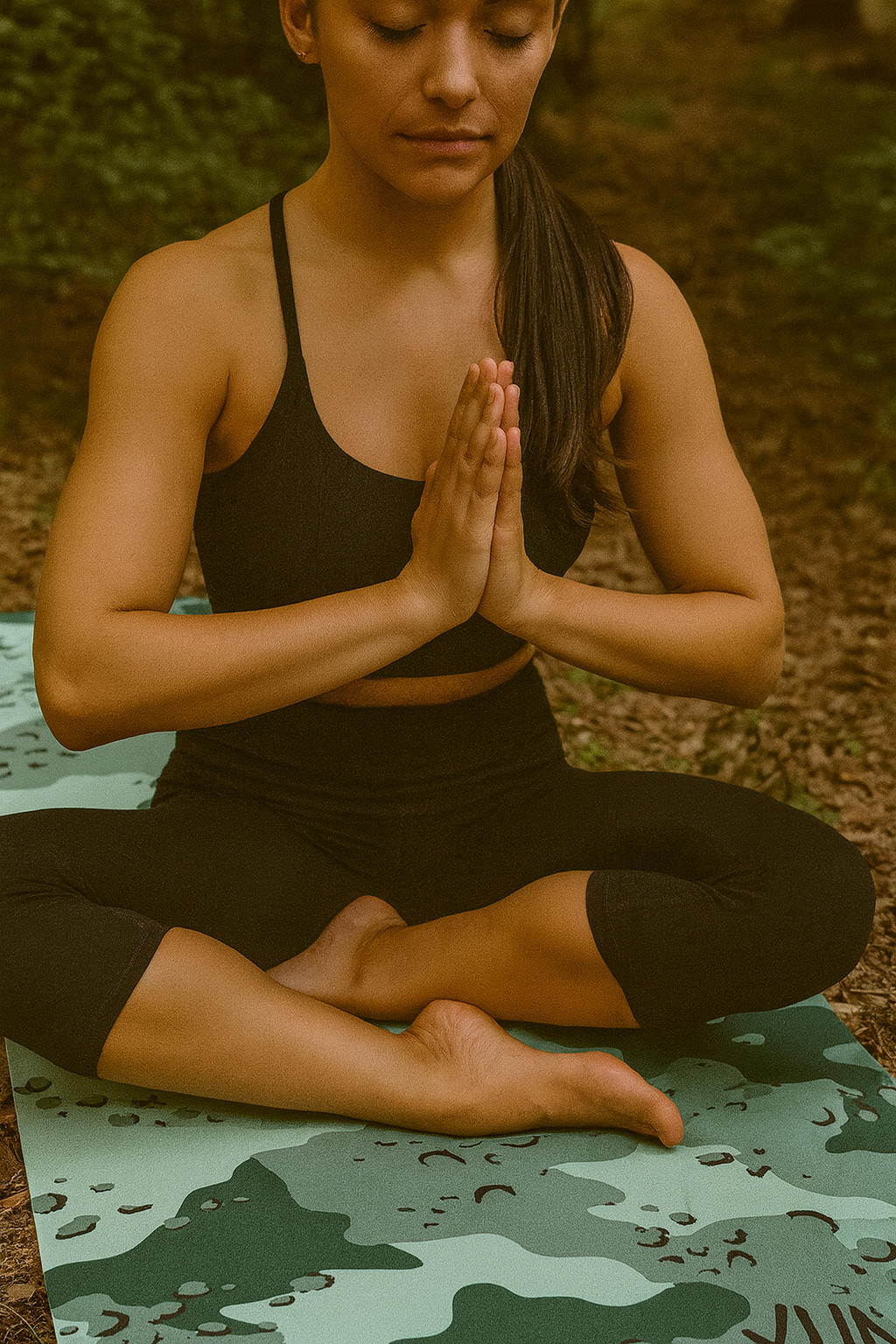 Woman in black athletic wear sitting in a yoga pose on a camouflage mat outdoors.
