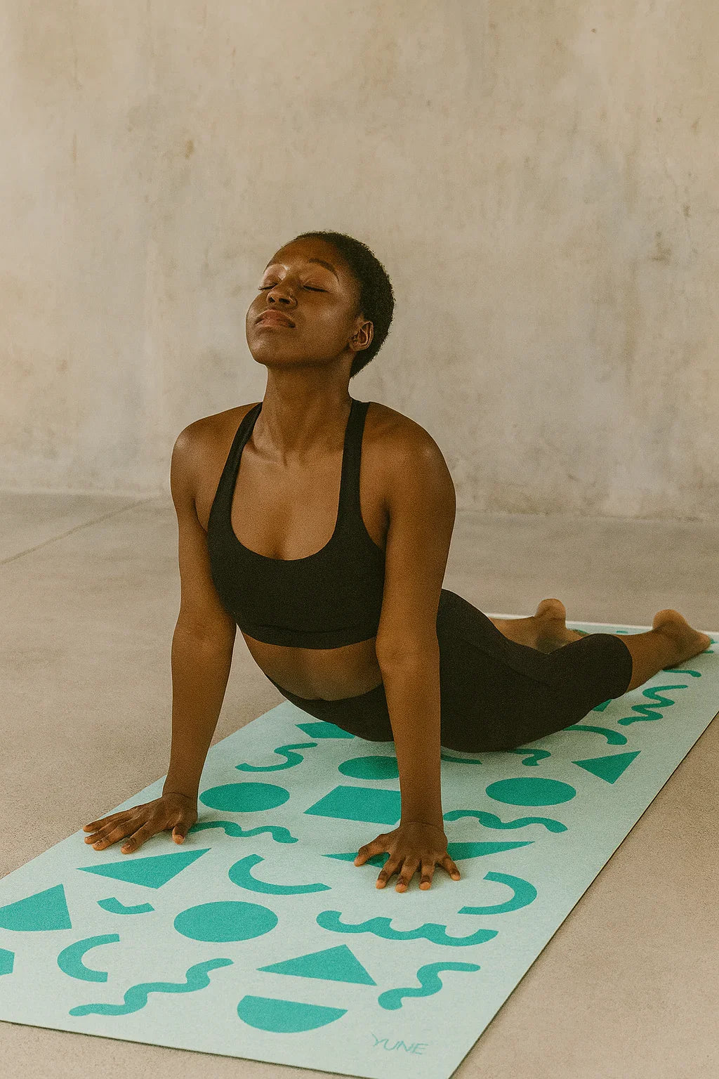 Woman practicing yoga on a mat with geometric patterns against a plain background
