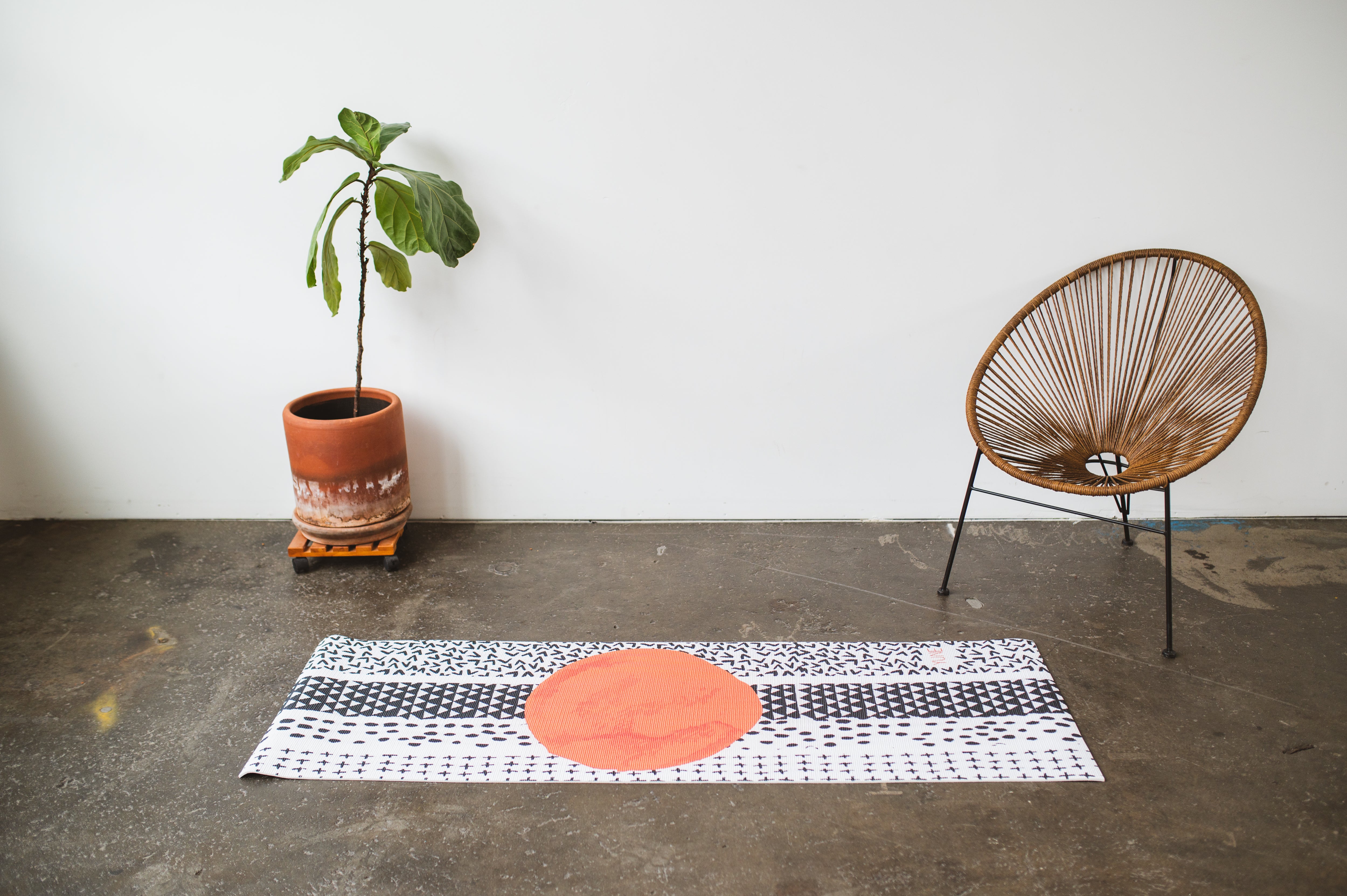 Yoga mat with a red circle on a concrete floor, accompanied by a plant and chair.