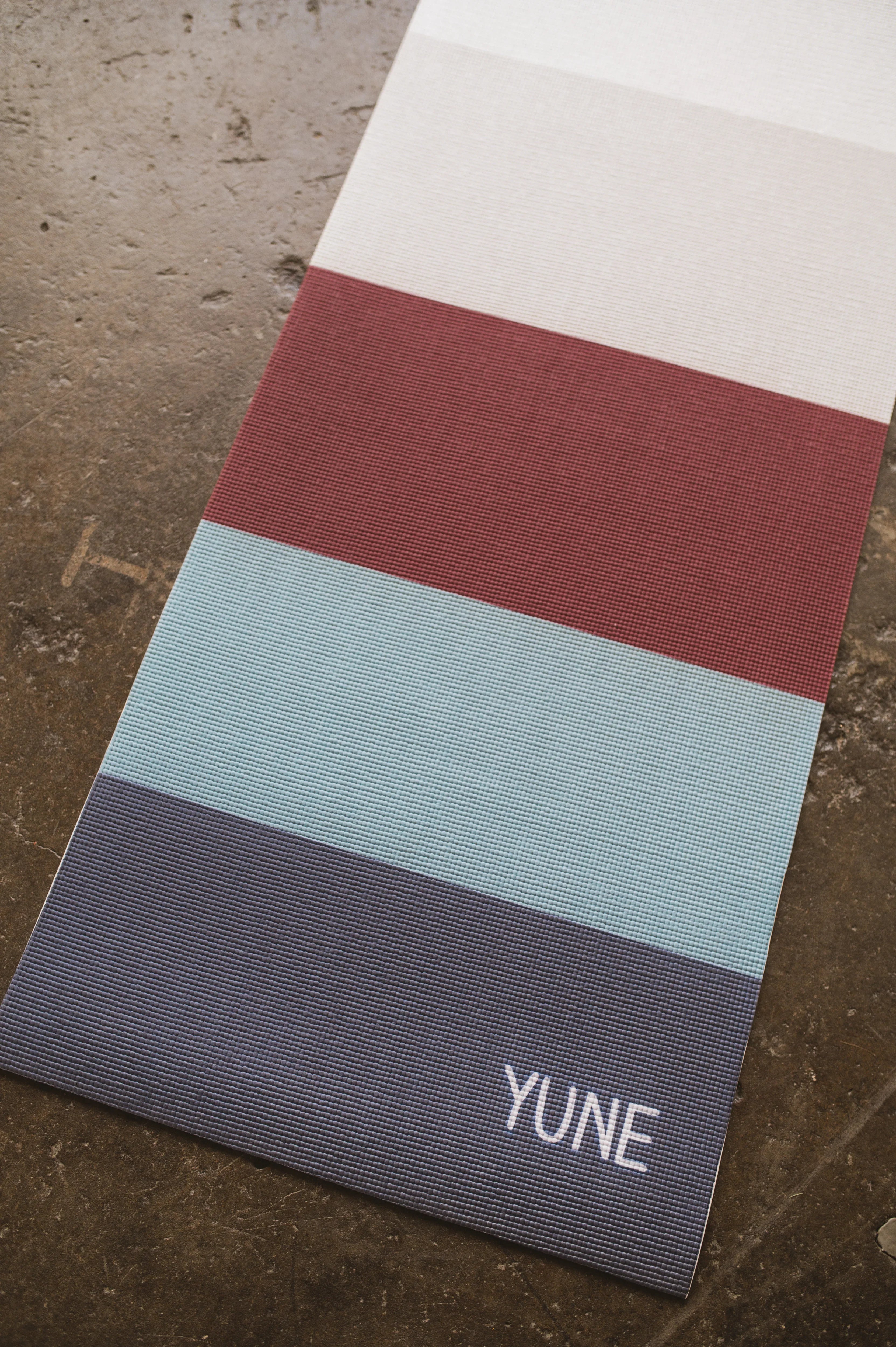 Yogamatte mit Farbverlauf von Weiß über Rot zu Blau und 'YUNE'-Logo.