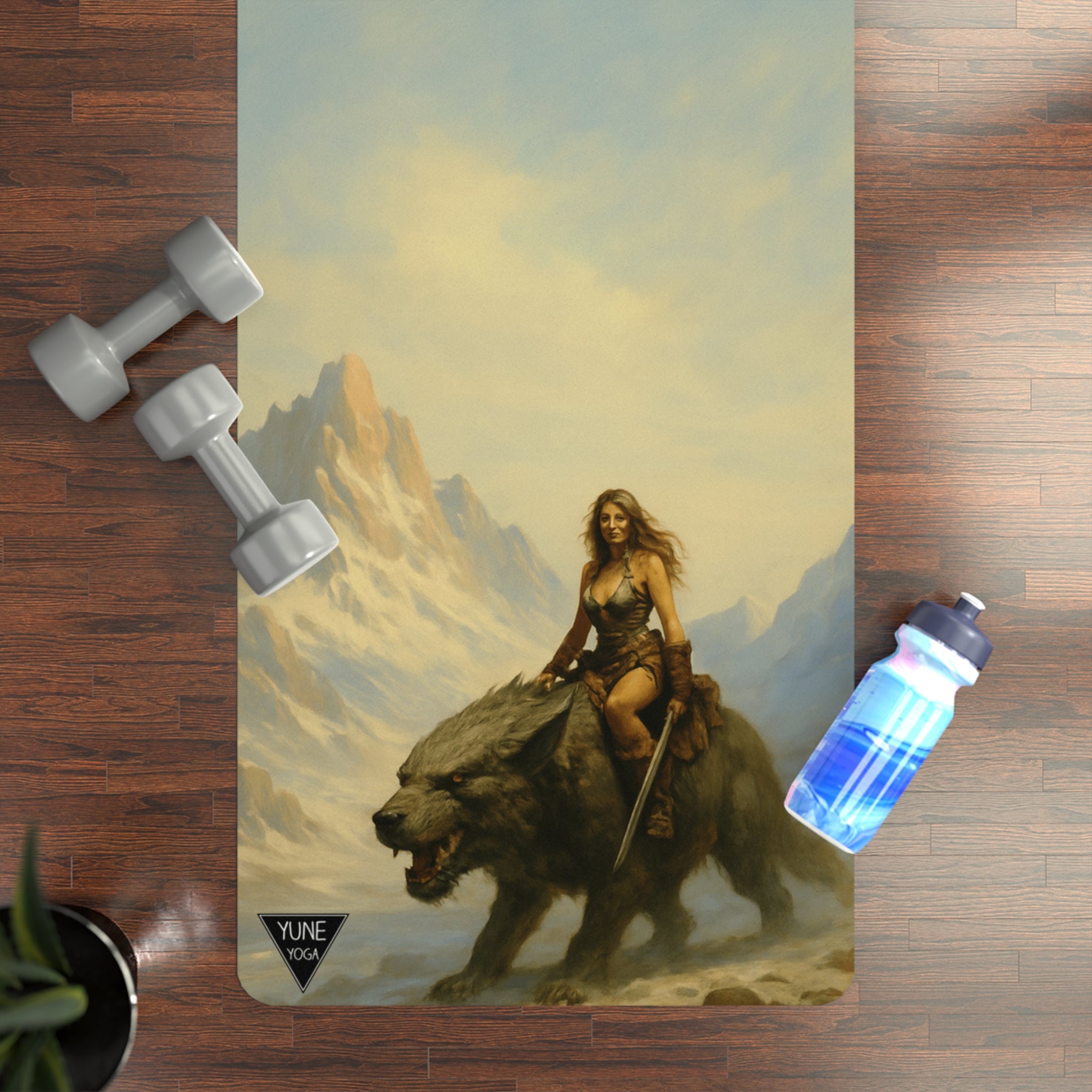Yoga mat with fantasy design of a woman riding a bear, placed on a wooden floor with dumbbells and a water bottle.