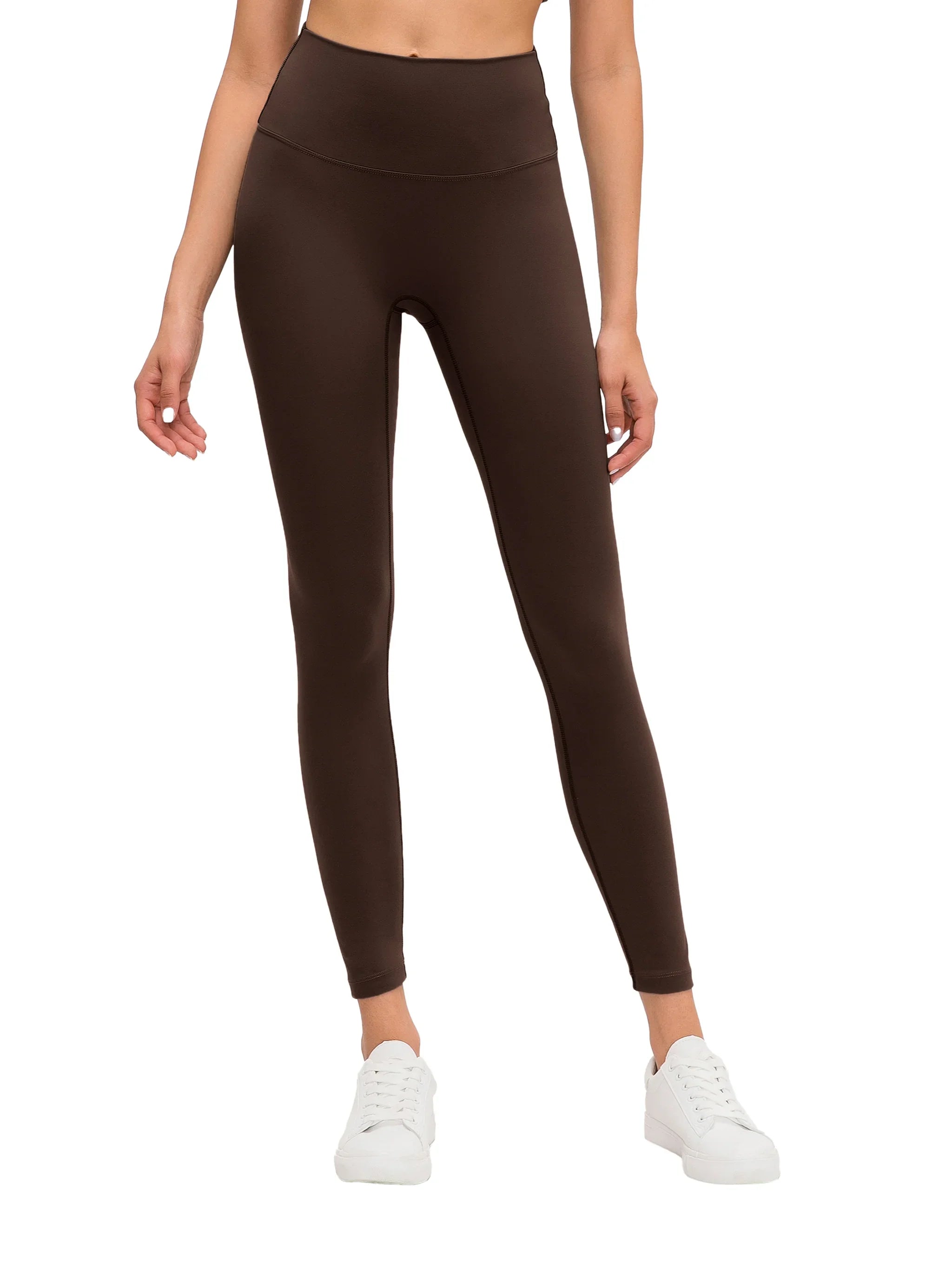 Woman wearing high-waisted brown yoga leggings and white sneakers on white background