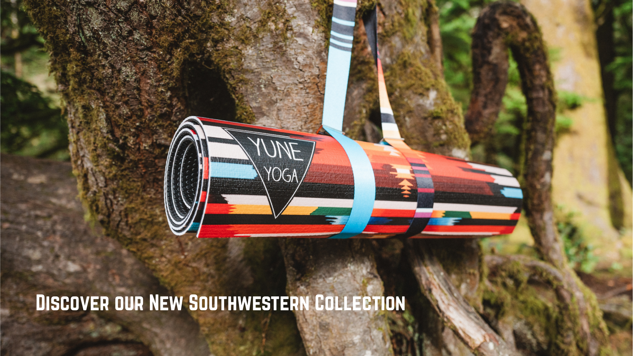 Colorful yoga mat with 'Yune Yoga' branding on a tree trunk, surrounded by nature.