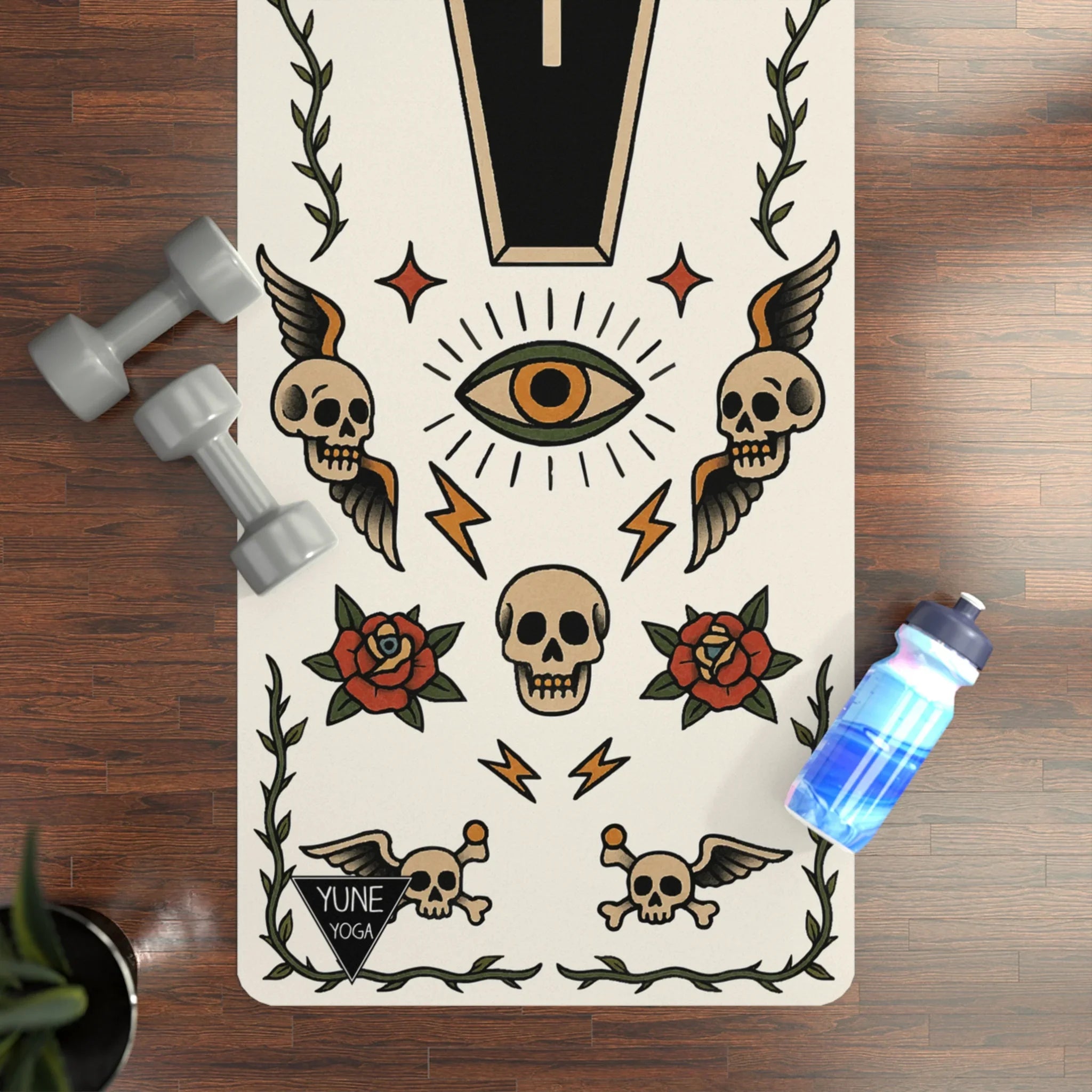 Yoga mat with tattoo designs on a wooden floor with dumbbells and a water bottle.